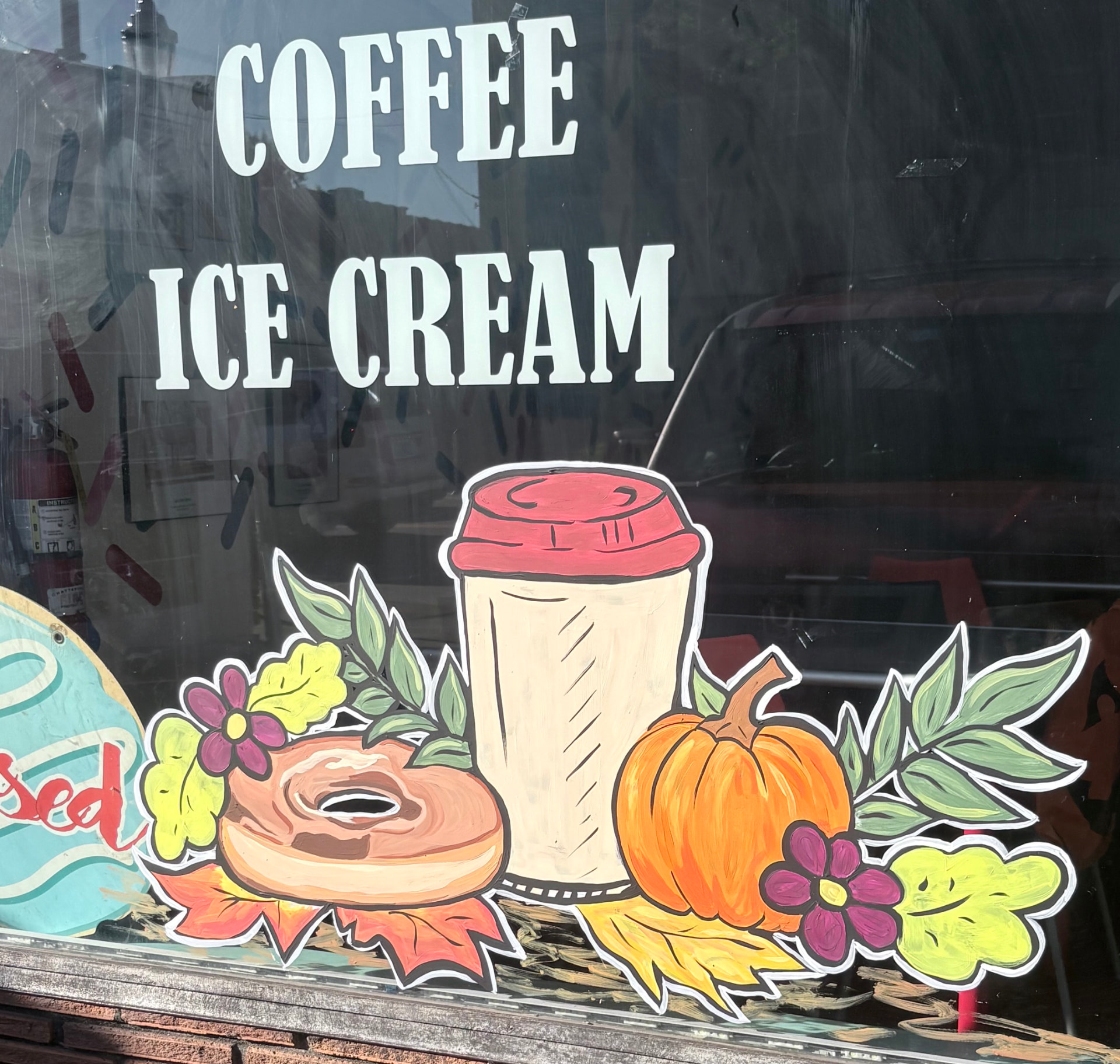 Fall window painting with a pumpkin, coffee cup, donut, flowers, and autumn leaves